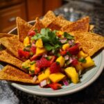 A close-up of a bowl of Delightful Fruit Salsa with fresh strawberries, mango, jalapeño, red onion, and cilantro, served with cinnamon chips.
