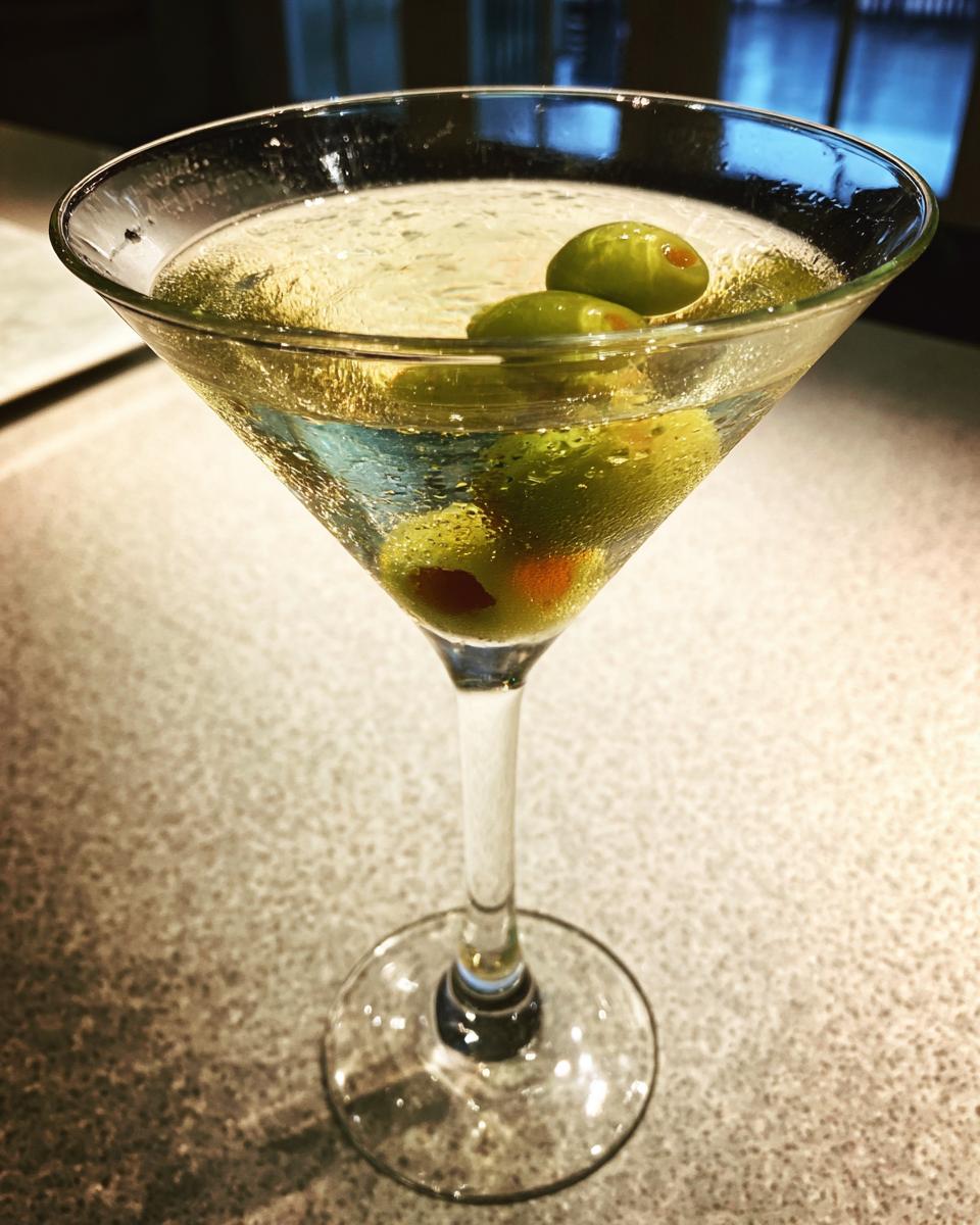 A classic Dirty Martini cocktail in a chilled martini glass, garnished with three green olives.