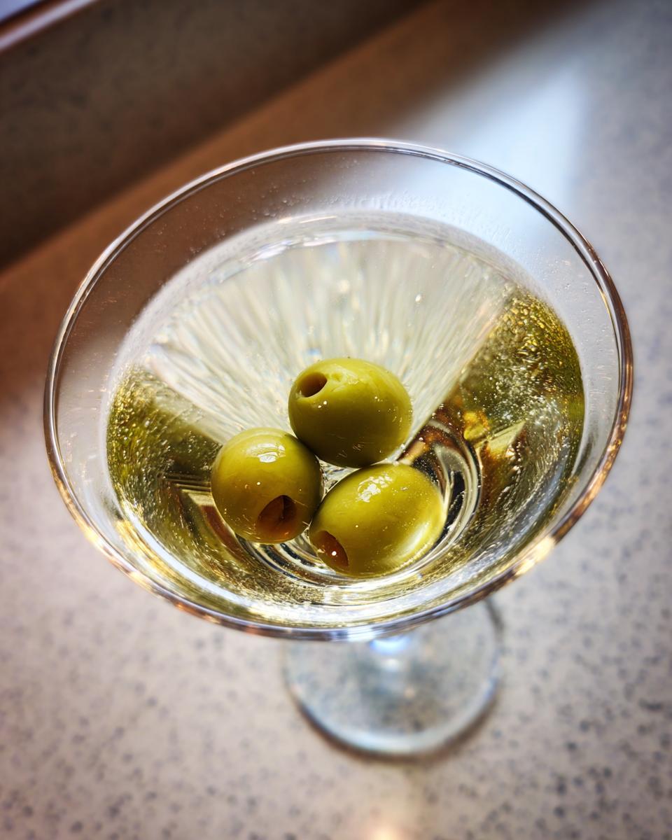 A classic Dirty Martini in a martini glass, garnished with three green olives.