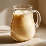 A glass pitcher filled with frothy, creamy Easy Homemade Oat Milk, ready to serve.