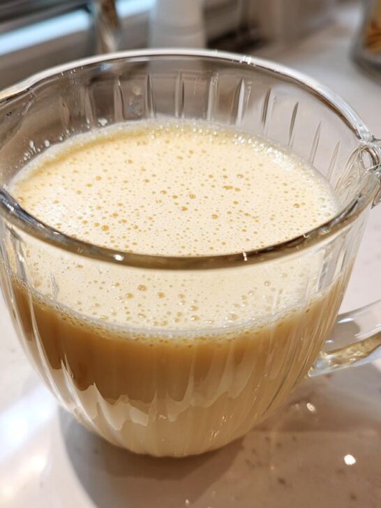 A clear glass pitcher filled with frothy, creamy Easy Homemade Oat Milk.