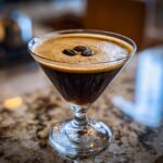 A close-up of a perfectly crafted Espresso Martini in a martini glass, topped with frothy crema and three coffee beans.