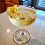 A refreshing French 75 cocktail in a coupe glass, garnished with a lemon twist and filled with bubbly champagne.