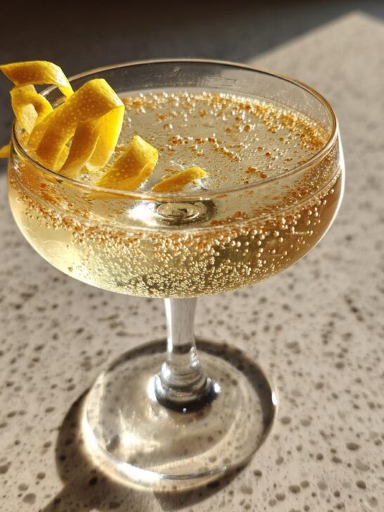 A refreshing French 75 cocktail in a coupe glass, garnished with a lemon twist and sparkling bubbles.
