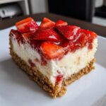 Close-up of a single serving of Fresh Strawberry Cheesecake Bars showing the graham cracker crust and strawberry topping.