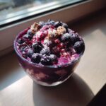 A refreshing bowl of frozen banana recipe topped with fresh blueberries, berry sauce, and crumbled cookies.