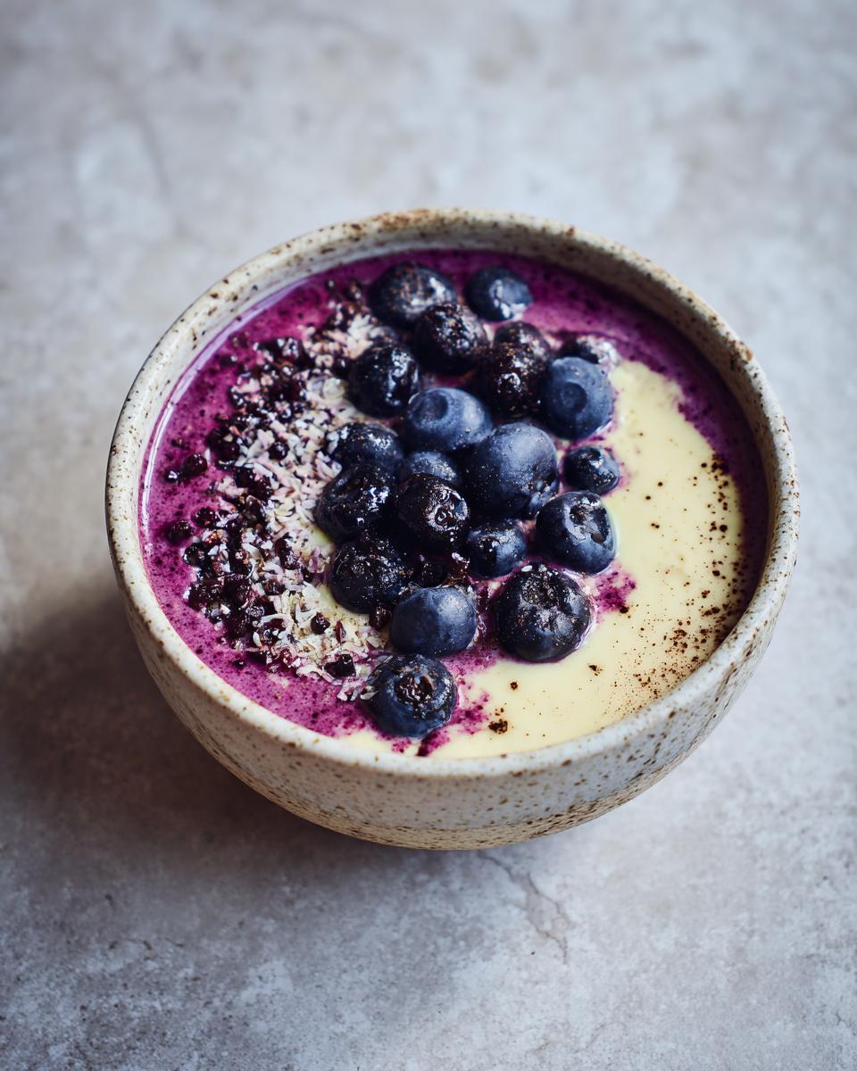 A vibrant frozen banana smoothie bowl topped with fresh blueberries and shredded coconut.