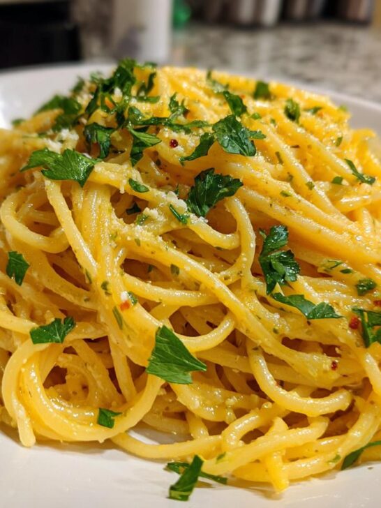A close-up of a white bowl filled with spaghetti tossed in a creamy garlic butter sauce and garnished with fresh parsley.