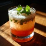 A close-up of a Gin Blossom Cocktail, a vibrant pink drink topped with crushed ice and fresh mint leaves.