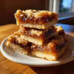 A stack of four gooey Butter Tart Squares with a shortbread base and crumb topping, bathed in warm sunlight.