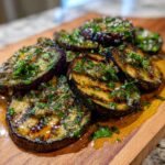 Close-up of tender grilled eggplant slices drizzled with a vibrant garlic vinaigrette and fresh herbs.
