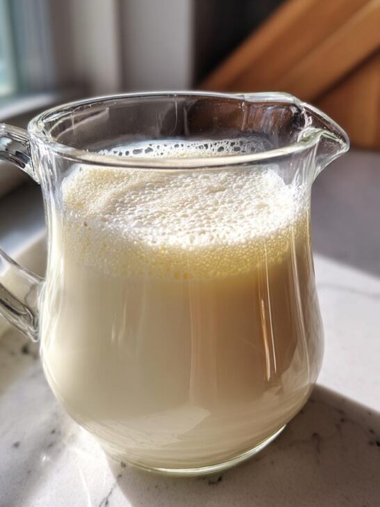 A glass pitcher filled with frothy, homemade creamy cashew milk, catching the sunlight.