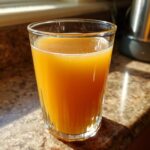A tall glass filled with vibrant Homemade Fresh Apple Juice, catching the sunlight.