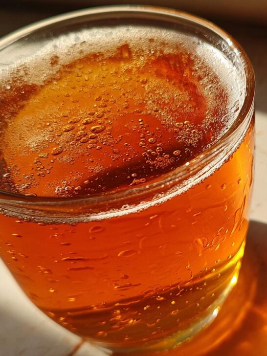A close-up of a glass filled with bubbly, amber-colored Homemade Fresh Apple Juice, catching the sunlight.