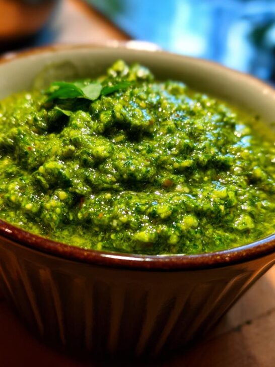 A close-up of vibrant green Homemade Pesto Sauce in a rustic bowl, garnished with a basil leaf.