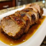 Juicy sliced Instant Pot Garlic Pork Tenderloin served in a savory sauce on a white platter.