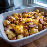 A close-up of Irresistible Cheesy Ranch Potatoes and Smoked Sausage in a white baking dish, topped with melted cheddar cheese.