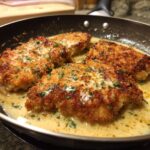 Four pieces of Irresistible Copycat Longhorn Parmesan Crusted Chicken sizzling in a creamy sauce in a pan, garnished with parsley.