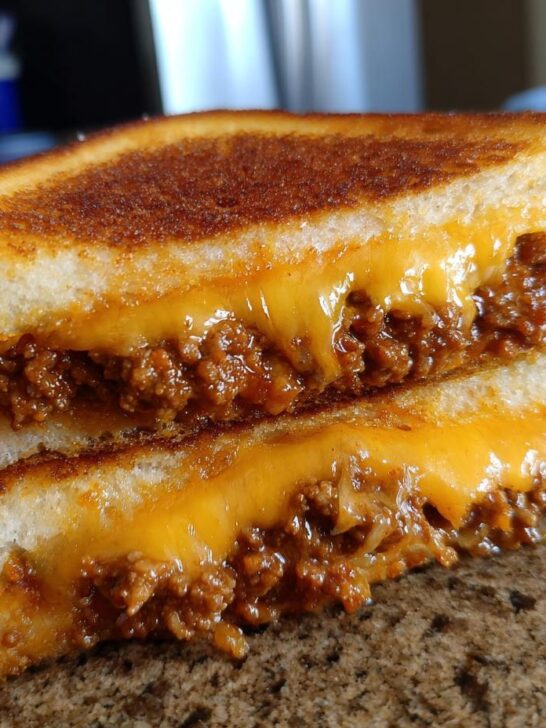 A close-up of two halves of an Irresistible Grilled Cheese Sloppy Joes sandwich, showcasing melted cheese and savory filling.