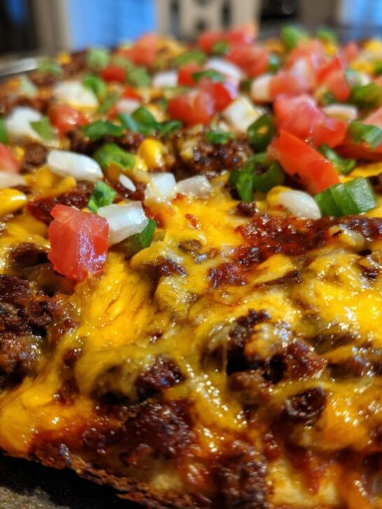 Close-up of an Irresistible Mexican Pizza Recipe topped with melted cheese, seasoned ground beef, tomatoes, onions, and green onions.