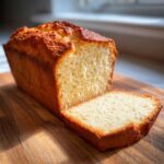 A freshly baked loaf of Irresistible Sour Cream Banana Bread, with one slice cut and resting on a wooden board.