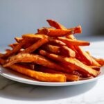 A close-up of a pile of crispy, golden-brown Irresistible Sweet Potato Fries on a white plate.