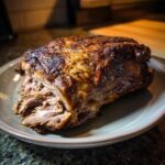 A perfectly cooked Juicy Slow Roasted Lamb Shoulder, with tender, shredded meat visible on a light grey plate.