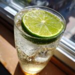A close-up of a Kansas City Ice Water Cocktail in a glass, garnished with a lime slice and filled with ice and bubbles.