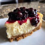 Close-up of a slice of creamy Lemon Cheesecake Blueberry Compote on a white plate.