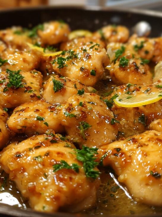 Close-up of tender Lemon Chicken with Lemon Butter Sauce, garnished with fresh parsley and lemon slices, in a skillet.