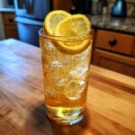 A tall glass filled with ice and a golden Lynchburg Lemonade Cocktail, garnished with two lemon slices.