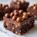 A decadent square of Malteser Slice, featuring a fudgy base mixed with crunchy bits, topped with chocolate ganache and whole Maltesers.