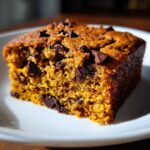 Close-up of a moist, square slice of Pumpkin Chocolate Chip Cake studded with dark chocolate chips on a white plate.