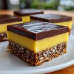 A close-up of one square Nanaimo Bar showing the three distinct layers: crumbly base, bright yellow custard filling, and dark chocolate topping.