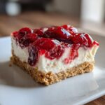 A close-up of one square serving of No Bake Cherry Cheesecake Bars on a white plate.
