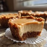 Close-up of a No Bake Peanut Butter Cheesecakes bite showing creamy filling and graham cracker crust, topped with caramel.