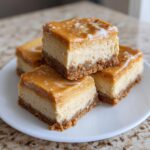 Four rich Peanut Butter Cheesecake Squares stacked on a white plate with a caramel topping.