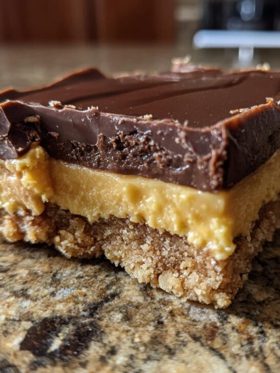 A close-up view of a single serving of Peanut Butter Nanaimo Bars showing the three distinct layers: crumb base, creamy peanut butter filling, and chocolate topping.