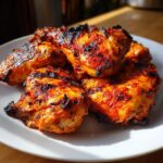 A close-up of several pieces of juicy Piri Piri Chicken, grilled to perfection with a spicy red marinade and char marks.