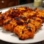 A plate piled high with perfectly grilled Piri Piri Chicken pieces, showcasing their vibrant orange-red marinade and charred edges.