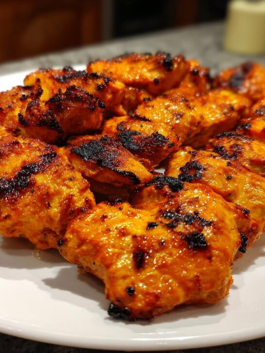 A plate piled high with perfectly grilled Piri Piri Chicken pieces, showcasing their vibrant orange-red marinade and charred edges.