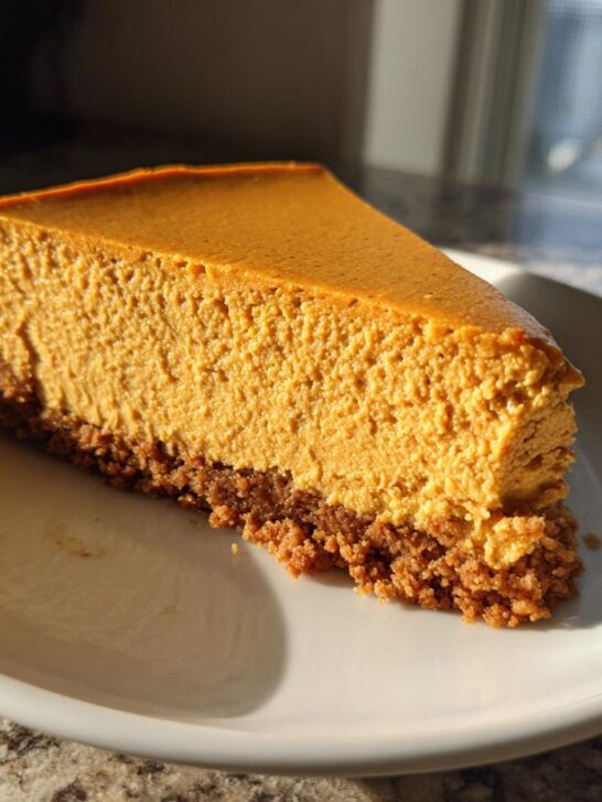 A thick slice of creamy Pumpkin Cheesecake with a graham cracker crust on a white plate.