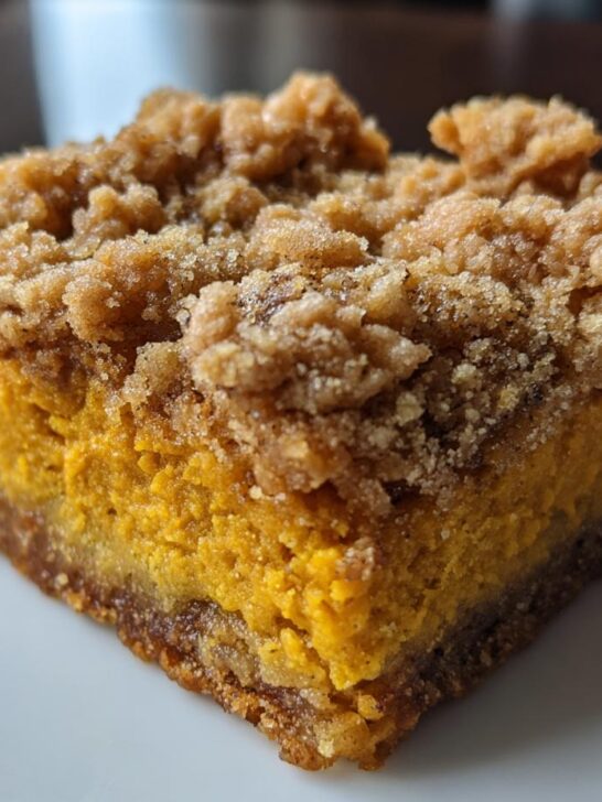 A close-up view of a single serving of rich, orange Pumpkin Streusel Bars with a thick, crumbly topping.