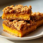 Close-up of two stacked Pumpkin Streusel Bars showing the bright orange pumpkin layer and thick brown sugar crumb topping.