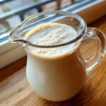 A glass pitcher filled with frothy, creamy quinoa milk, perfect for a dairy-free alternative.