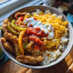 A close-up of a delicious Ranch Chicken Fajita Bowl, featuring seasoned chicken strips, bell peppers, rice, shredded cheese, salsa, and sour cream.