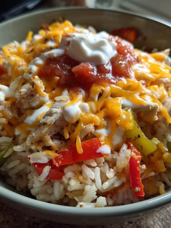 A close-up of a Ranch Chicken Fajita Bowl filled with rice, shredded chicken, bell peppers, cheese, salsa, and sour cream.