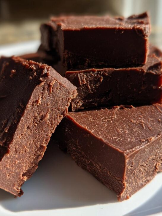 Close-up of rich, dark chocolate Fantasy Fudge cut into squares stacked on a white plate.