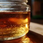 Close-up of golden simple syrup in a glass jar, with small bubbles and light reflections.