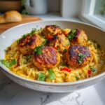 A close-up of Spicy Curry Vegan Meatballs Orzo, garnished with fresh cilantro and red chili peppers.